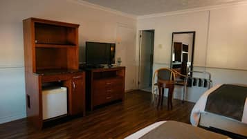 A hotel room with a wooden desk, a television, a chair, and a bed.