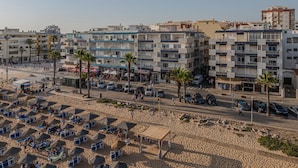 Un'area urbana costiera con edifici a più piani, una spiaggia sabbiosa con lettini e un cielo sereno.