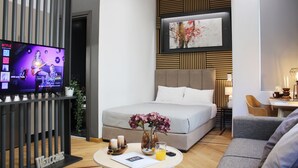 Una camera d'albergo moderna con un letto, un divano, una TV e un tavolino con un vaso e un bicchiere di succo d'arancia.