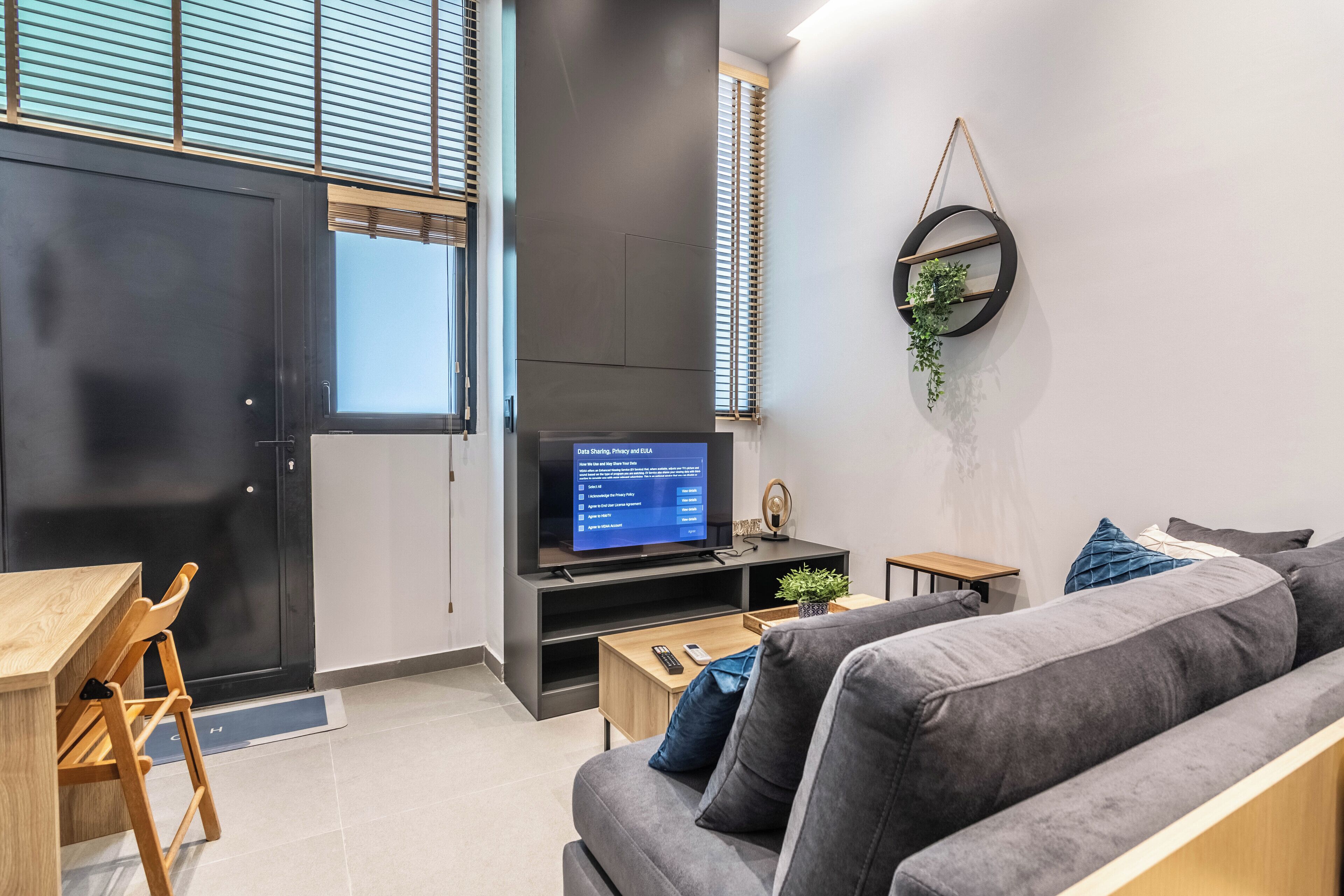Un soggiorno moderno con un divano grigio, un tavolo da pranzo in legno e una TV che mostra un menù.