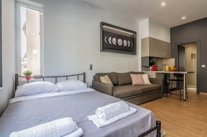 Una habitación de hotel moderna con una cama grande, un sofá, una pequeña cocina y una mesa de comedor.