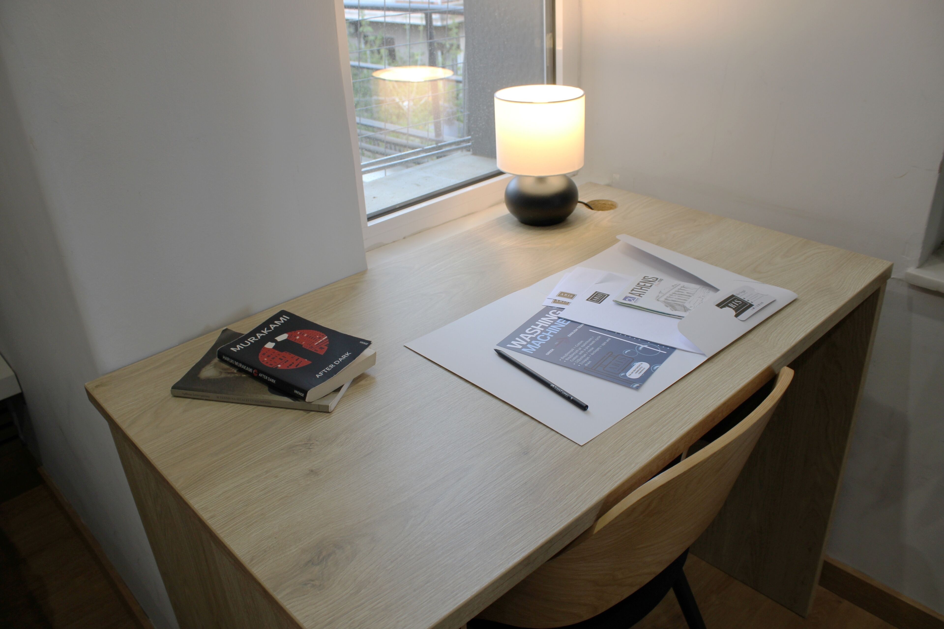 A wooden desk with a lamp, a book titled "Murakami," and documents.