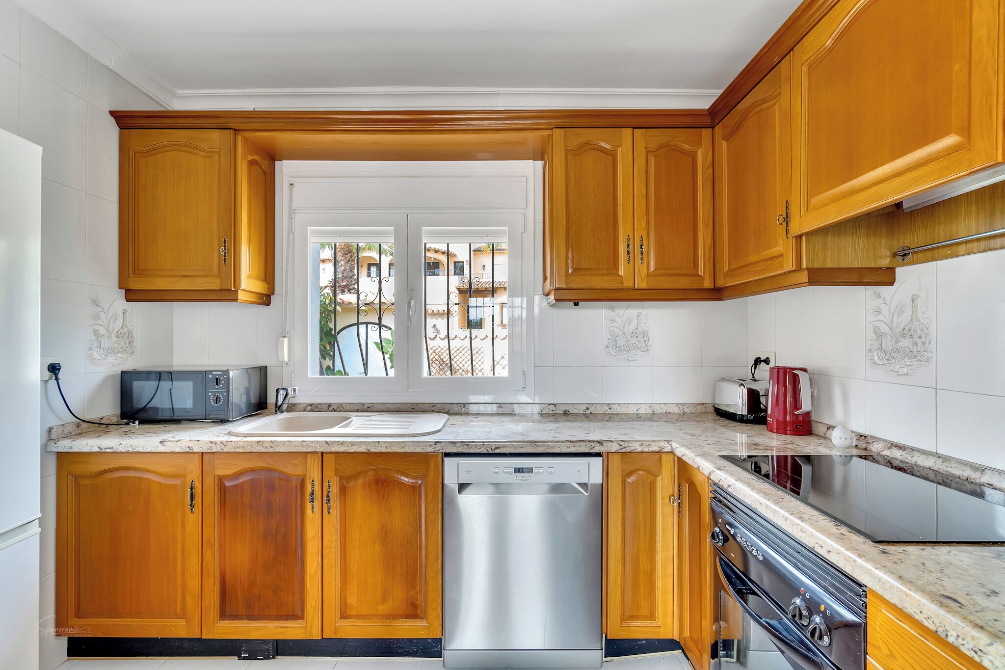 Una cocina con gabinetes de madera, lavavajillas, estufa y microondas.