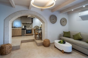 A modern living room with a sofa, coffee table, and a kitchen visible through an archway. - Conaleni - Concona houses (Megalo Metochi)