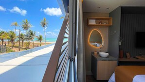 A hotel room with a large window overlooking a beach, a round mirror, a sink, and a TV. - Acqua Tambaú Prime - By Almare (João Pessoa)