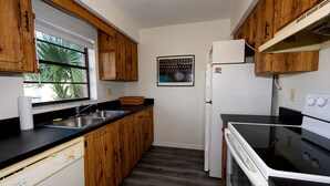 A compact kitchen with wooden cabinets, a stainless steel sink, a white refrigerator, and a black stove. - Spacious, privet entry retreat 2 min walk to Worlds Famous Beach! (Daytona Beach Shores)