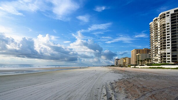 A beach with a sandy shore and a row of multi-story buildings in the background. - Spacious, privet entry retreat 2 min walk to Worlds Famous Beach! (Daytona Beach Shores)