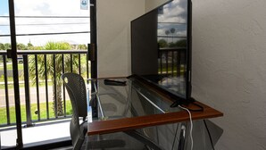 A balcony with a glass desk, a chair, a TV, and a remote control. - Spacious, privet entry retreat 2 min walk to Worlds Famous Beach! (Daytona Beach Shores)