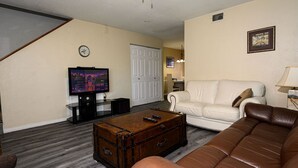 A living room with a television, a white sofa, a brown leather couch, and a wooden chest. - Spacious, privet entry retreat 2 min walk to Worlds Famous Beach! (Daytona Beach Shores)