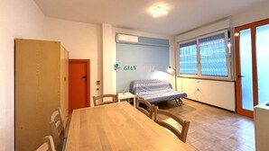 Quarto com mesa e cadeiras de madeira, cama com manta estampada, janela com persianas e porta.