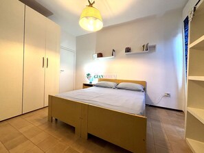 Une chambre avec un lit en bois, une table de chevet, une étagère remplie de livres et un panneau accroché au mur.