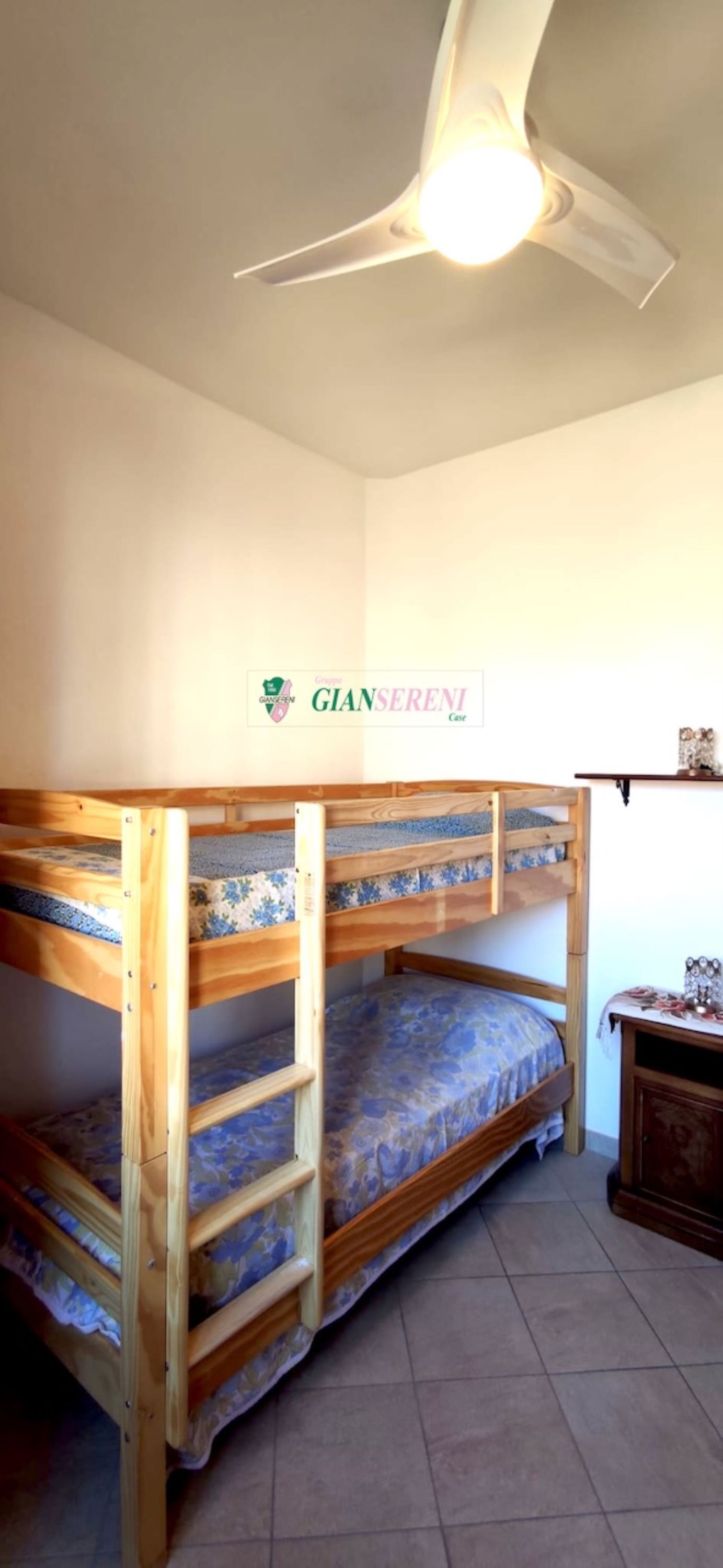 Habitació amb lliteres, ventilador de sostre i logotip fixat a la paret.