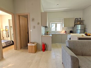A modern kitchen with a built-in stove, a refrigerator, and a sink. There is a dining area with a table and a sofa. - Olive garden farmhouse 1 (Sperchogia)