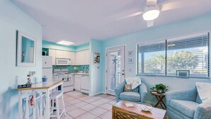 A living room with a sofa, coffee table, and a kitchen area with cabinets and appliances. - Sand Castle Serenity Studio - Sleeps 4 - Steps to the Beach - No Extra Fees (Panama City)