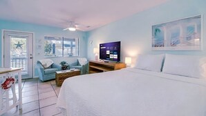 A hotel room with a bed, a desk, a chair, a TV, and a painting on the wall. - Sand Castle Serenity Studio - Sleeps 4 - Steps to the Beach - No Extra Fees (Panama City)