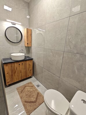 Een moderne badkamer met een ronde spiegel, een houten kastje, een witte wastafel en een toilet.