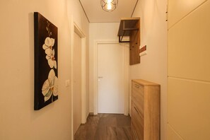 A hallway with a wooden cabinet, a white door, and a wall-mounted shelf. - Designer Apartment in the Pines | San Pietro (Plazhi San Pietro)