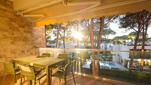 Un balcone con tavolo e sedie, vista su una piscina e alberi.