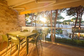 A balcony with a table and chairs, overlooking a pool and trees. - Designer Apartment in the Pines | San Pietro (Plazhi San Pietro)