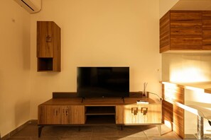 A modern living room with a flat-screen TV on a wooden entertainment unit, a built-in cabinet, and a small table with a remote control. - Designer Apartment in the Pines | San Pietro (Plazhi San Pietro)