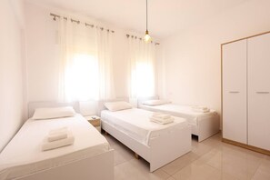 Een moderne, goed verlichte hotelkamer met drie bedden, een kledingkast en een groot raam met gordijnen.