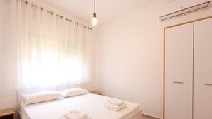 Un dormitorio minimalista con cama, mesita de noche, armario y lámpara colgante.