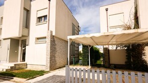 Un immeuble résidentiel moderne doté d’un espace extérieur aménagé et couvert, ainsi que d’une clôture blanche en bois.