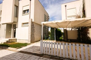 Ein modernes Wohngebäude mit überdachter Außenbereich-Sitzgelegenheit und weißem Zaun.