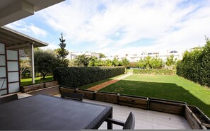 Eine Terrasse mit Tisch und Stühlen, eine Holzbank und ein gepflegter Rasen.
