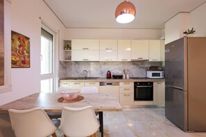 Une cuisine moderne avec des meubles blancs, une table à manger en bois et un réfrigérateur en acier inoxydable.