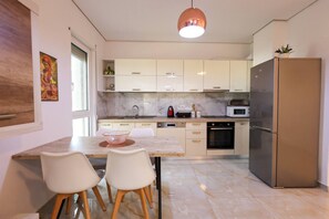 A modern kitchen with white cabinets, a stainless steel refrigerator, and a marble countertop. There is a dining table with chairs and a pendant light above it. - Sanpietro Vacation Apartment 048 (Plazhi San Pietro)