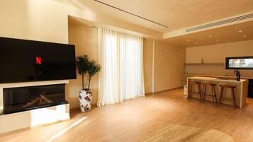 A modern living room with a flat-screen TV, a fireplace, a dining area with bar stools, and a large window with curtains.