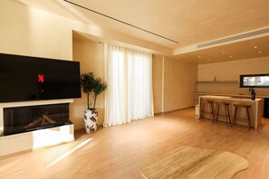 Uma sala de estar moderna com televisão de tela plana, lareira, área de jantar com banquetas e uma janela grande com cortinas.