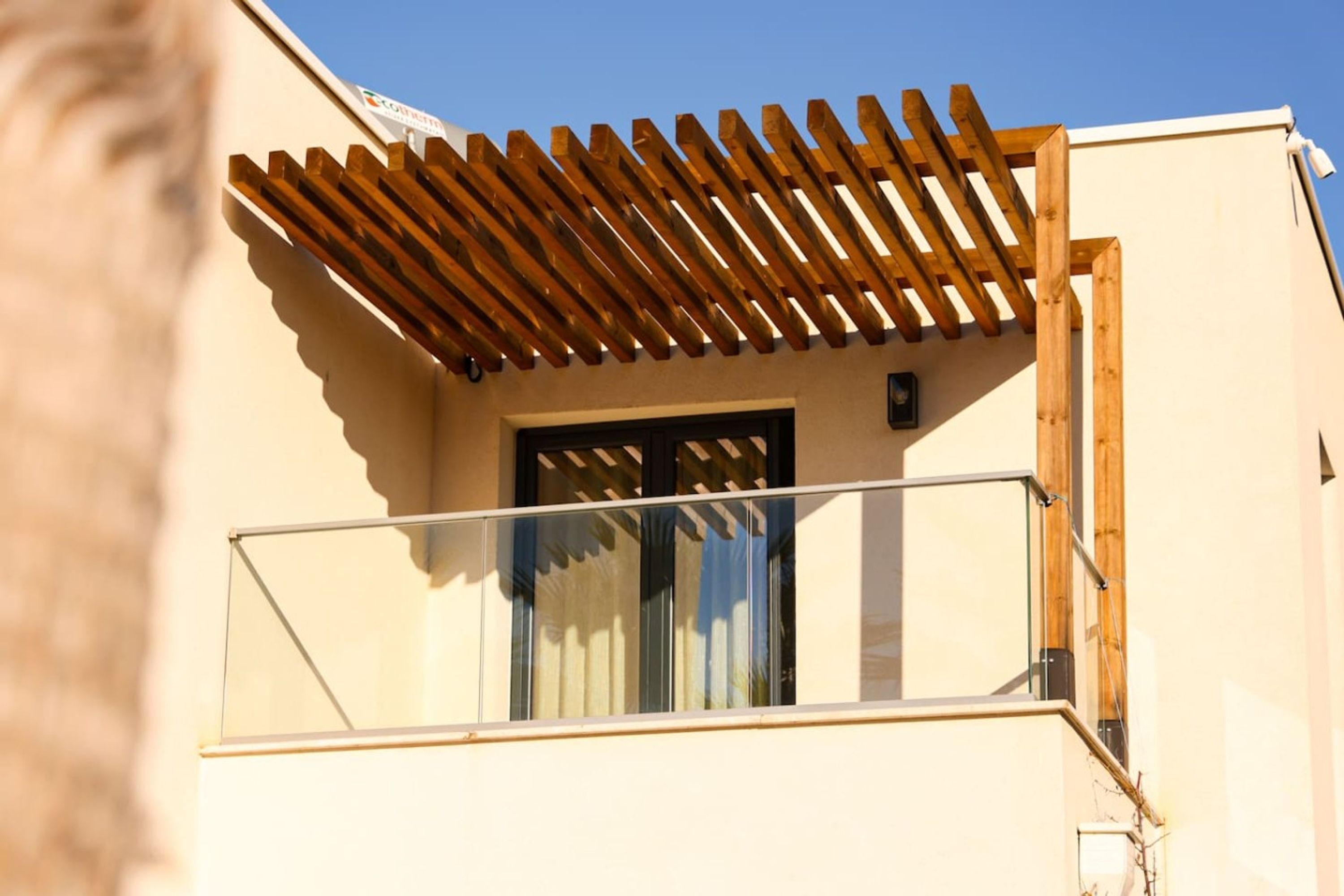 A balcony with a wooden pergola, a glass railing, and a door with a window.