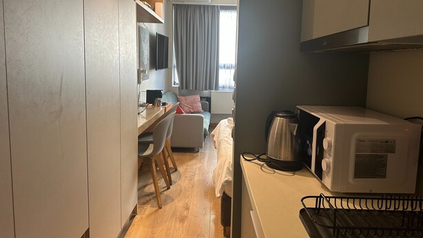 Cozinha compacta com micro-ondas, chaleira e pequena área de refeições com mesa e cadeiras.