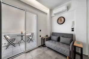 Un salon moderne avec un canapé gris, une petite table en bois et une porte en verre donnant sur un balcon équipé de deux chaises.