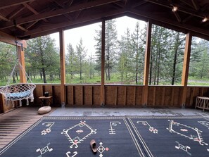 Eine Holzterrasse mit einem Hängesessel, einem gemusterten Teppich und Blick auf einen Wald.
