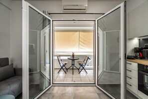 Un intérieur moderne avec une porte-fenêtre coulissante donnant sur un balcon équipé d’une table et de chaises, d’un canapé et d’un coin cuisine.