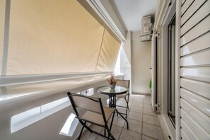 A balcony with a table and chairs, a beige awning, and a sliding door. - Nicol studio by Cretanhouses (Iraklio)