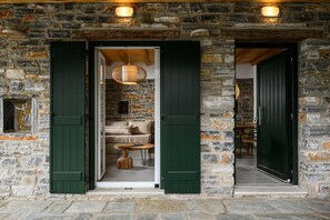 Ein Steinhaus mit grünen Fensterläden und einem gemütlichen Innenraum, der ein Sofa, einen runden Holztisch und eine Pendelleuchte zeigt.