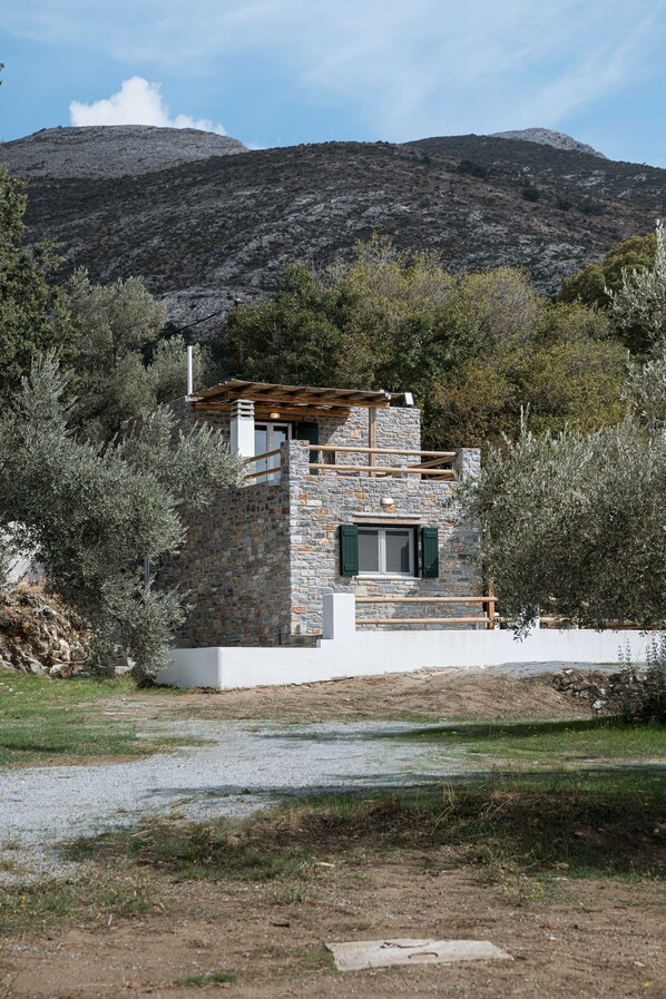Ein Steinhaus mit einer Holzdar Terrasse, umgeben von Olivenbäumen und einer Bergkulisse.