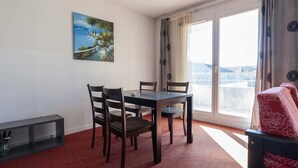 A dining area with a table and chairs, a painting on the wall, and a view through a window. - Charming apartment for 4 people near shops (Grasse)
