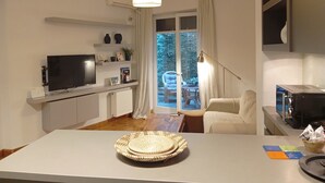 Ein modernes Wohnzimmer mit Flachbildfernseher, einem Esstisch mit gewebtem Korb und Blick auf einen Balkon mit Stuhl.