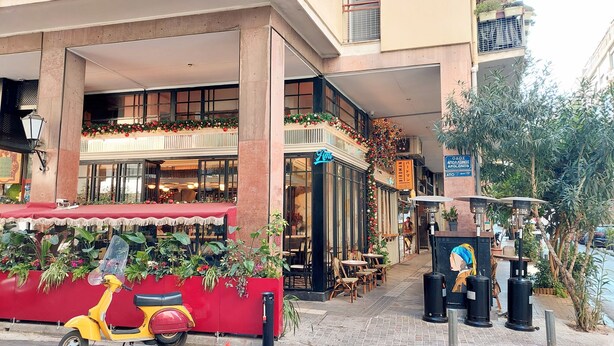 Straßenansicht eines Restaurants namens 'Ami' mit Außenbestuhlung und einer roten Markise.