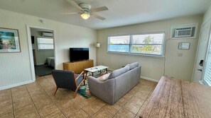 Ein Wohnzimmer mit einer Couch, einem Fernseher, einem Deckenventilator und einem Fenster mit Jalousien.