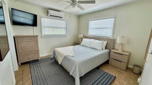A bedroom with a bed, bedside tables, a TV, and a ceiling fan. - SunShell 3 - Steps from Sand (Fort Myers)