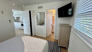 A bedroom with a bed, a television mounted on the wall, and a view of the kitchen and bathroom through an open door. - SunShell 3 - Steps from Sand (Fort Myers)