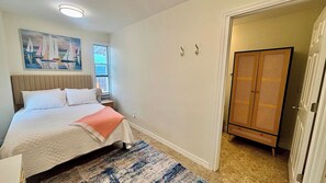 Ein Schlafzimmer mit Bett, Fenster, Gemälde, Kleiderschrank und Tür.