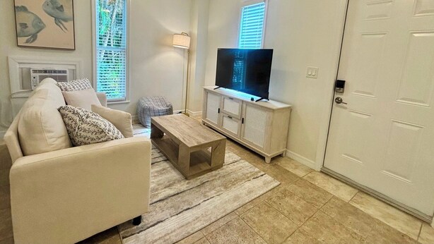 Ein Wohnzimmer mit einer Couch, einem Couchtisch, einem Fernseher auf einem weißen Schrank, einer Lampe und einer Tür.