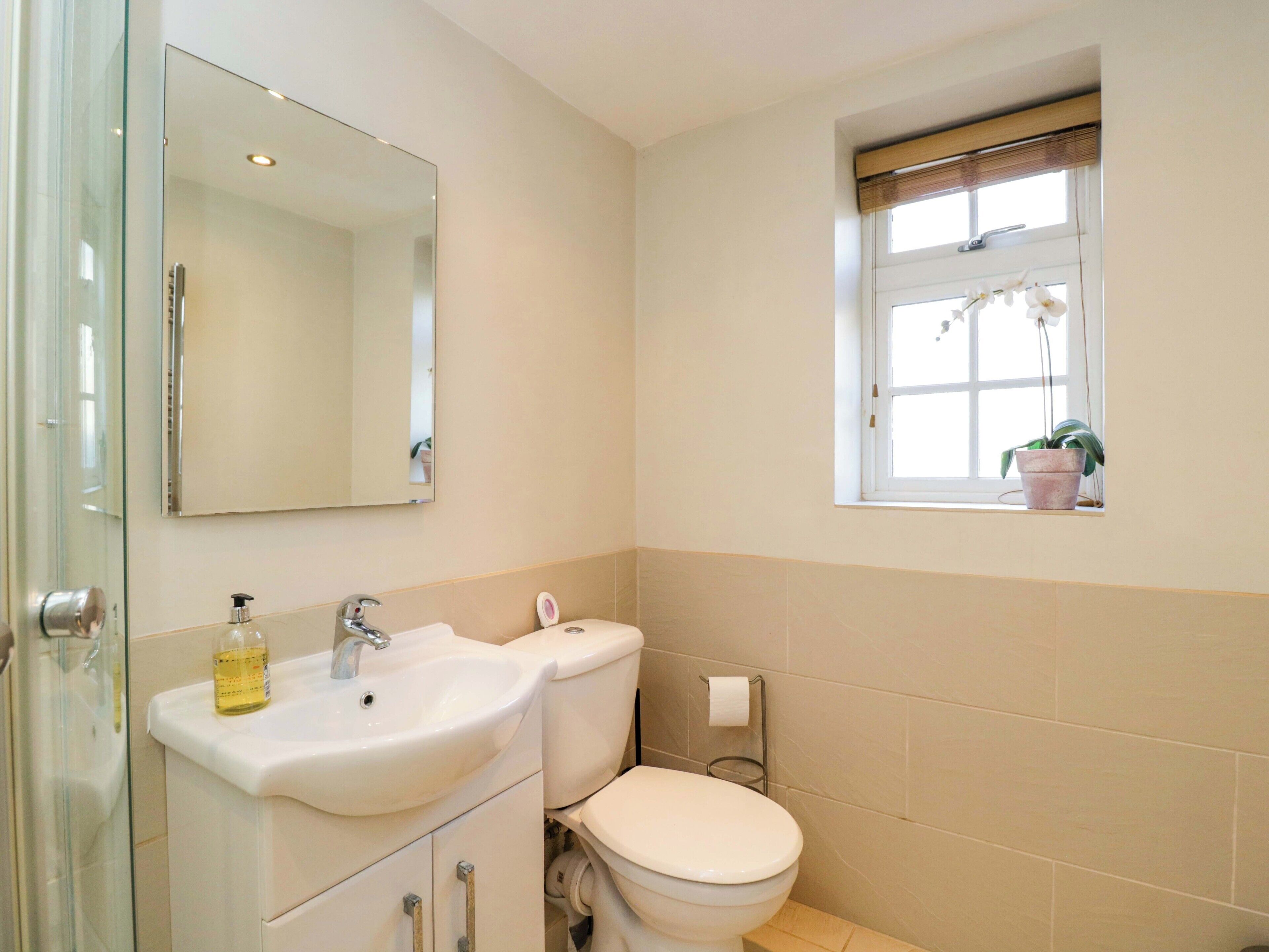 Een badkamer met een wastafel, toilet en een raam met een bloempot.